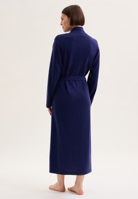 Lungo abito blu navy con colletto a scialle, cintura e maniche lunghe. Texture morbida e design minimalista; arriva fino alle caviglie.