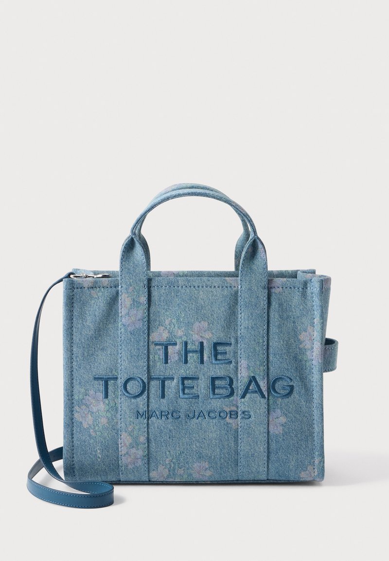 Μπλε τσάντα το tote από τζιν με floral σχέδιο, κοντές λαβές και ρυθμιζόμενο μπλε λουρί, με την επωνυμία "THE TOTE BAG MARC JACOBS" στο μπροστινό μέρος.