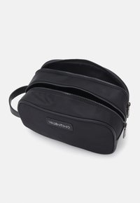 Čierna nylónová toaletná taška s dvoma zipsovými priehradkami, plochý dizajn a nášivka s logom Valentino. Hladký povrch a kompaktný tvar.