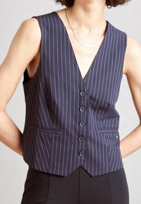 Marinblå, randig väst med V-ringning, fem knappar fram och två fickor. Tillverkad av ett slätt tyg, skräddarsydd passform med en skarp design.