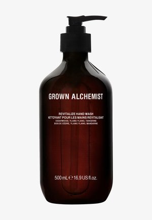 Ciemnozłota szklana butelka z czarną pompką, oznakowana "Grown Alchemist Revitalize Hand Wash", z białym tekstem i nazwami składników kwiatowych.