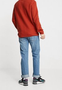 Red knit sweater, light blue denim jeans with cuffs, and black sneakers with teal and purple accents. Simple, casual outfit.
