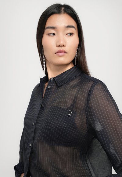 Black, sheer button-up shirt with vertical white stripes, a chest pocket with a pin detail, and long sleeves. Smooth texture and lightweight fabric.
