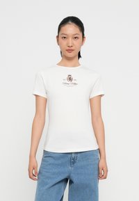 Tricou alb din bumbac, cu mânecă scurtă, având un design imprimat cu un logo maro și o coroana pe piept. Stil simplu, croit pe corpo.