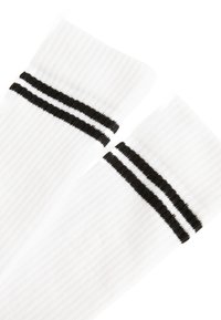 Calzini bianchi a costine con due strisce orizzontali nere sulla parte superiore. Il materiale sembra morbido ed elastico, offrendo una vestibilità aderente.