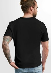 Schwarzes kurzärmliges T-Shirt mit klassischem Rundhalsausschnitt, aus glattem Stoff gefertigt, mit sichtbaren Tattoo-Details am Arm und lässigen Jeans.