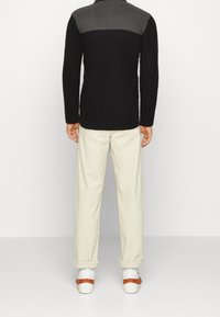Pull en textures noir et gris à manches longues, associé à un pantalon crème et des chaussures blanches avec des sangles marron.