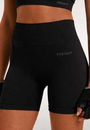 Nahaufnahme einer Person, die schwarze, hoch taillierte Sportshorts und ein passendes bauchfreies Oberteil mit fingerlosen Trainingshandschuhen trägt.