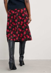 O fustă florală cu un fundal negru prezintă maci roșii mari și frunze verzi, asortată cu cizme negre din piele până la genunchi, cu toc.