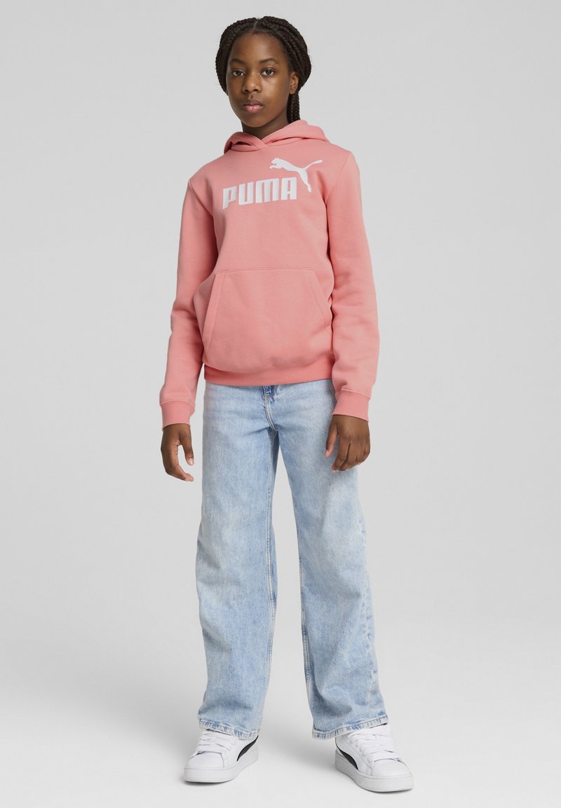 Felpa rosa con logo "PUMA" bianco, dotata di tasca frontale, abbinata a jeans a gamba larga di colore blu chiaro e sneakers bianche.