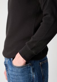 Svart langermet skjorte i waffle-strikk med ribbestrikkede mansjetter, sammen med blå denimjeans med klassisk lomme-design.
