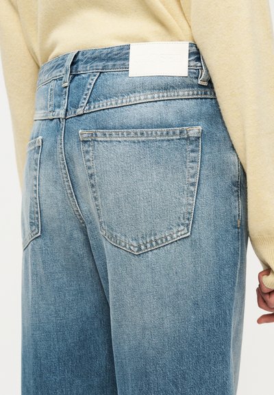 Vaqueros de mezclilla azul claro con cintura alta, con dos bolsillos traseros y una etiqueta crema en la cinturilla. Textura suave y ajuste relajado.