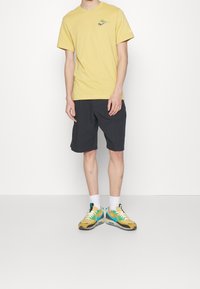 Yellow short-sleeve T-shirt with a printed logo, paired with dark shorts. Footwear features a yellow and teal design with white accents.