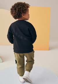 Svart sweatshirts med texturerad diagonallig rand, olivgröna cargo-byxor och vita sneakers, med elastiska mudd och patchfickor.