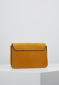 Borsa a tracolla gialla con motivo testurizzato, dotata di chiusura a patta liscia e cuciture a contrasto. Forma rettangolare compatta, realizzata in pelle.