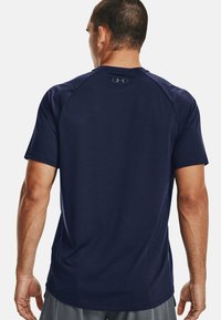 Tummansininen urheilut-paita, jossa on lyhyet hihat, sileä pinta ja pyöreä pääntie. Takana on hillitty brändilogot.