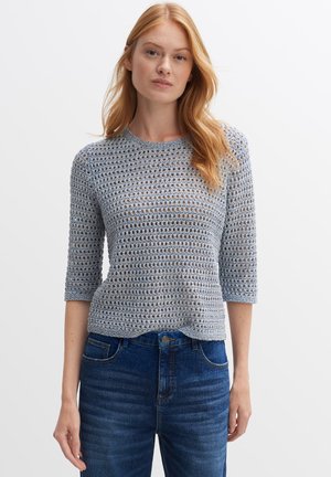 Top in maglia all'uncinetto azzurro chiaro con maniche a tre quarti, caratterizzato da un motivo aperto e scollatura rotonda, abbinato a jeans in denim blu scuro.