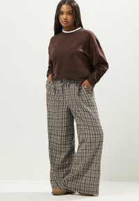 Brun kort sweatshirt tillsammans med vida, svartvita rutiga byxor. Byxorna har fickor och dragsko i midjan.