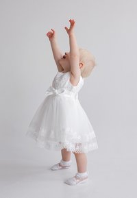 White dress with lace trim and pearl accents, featuring a fitted bodice and tulle skirt. Circular white shoes with lace details.
