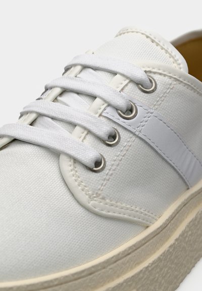 Λευκό πάνινο αθλητικό παπούτσι με λευκά κορδόνια, ασημένιες τρύπες κορδονιών, λευκή πλαϊνή ρίγα και υφασμένο λαστιχένιο πέλμα σε ανοιχτό εκρού χρώμα.