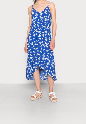 Blauwe bloemen midi-jurk met spaghetti bandjes, witte madeliefjes, uitlopende zoom en een getailleerde taille. Gecombineerd met witte sandaaltjes met banden.
