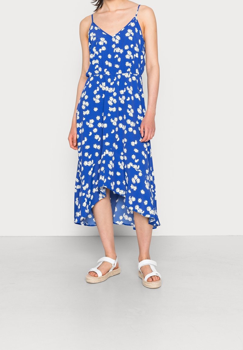 Vestido midi azul con estampado de flores, tirantes finos, margaritas blancas, dobladillo acampanado y cintura ajustada. Combinado con sandalias blancas de tiras.