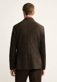 Blazer marrone con texture e un sottile motivo a quadretti, con spacco singolo. Vestibilità sartoriale con maniche lunghe e polsini abbottonati, visto da dietro.