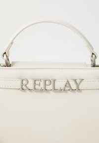 Sac à main en synthétique beige au design structuré, doté d'une anse supérieure et d'un logo argenté "REPLAY" affiché de manière proéminente sur le devant.
