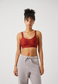 Roter Sport-BH aus glattem Material mit breiten Trägern und Logodetail. Kombiniert mit hellgrauen Jogginghosen, die eine lockere Passform zeigen.