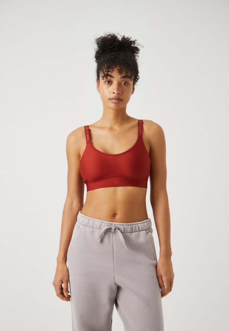 Roter Sport-BH aus glattem Material mit breiten Trägern und Logodetail. Kombiniert mit hellgrauen Jogginghosen, die eine lockere Passform zeigen.