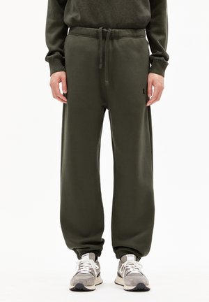 Olive green joggers with a drawstring waist, elastic cuffs, soft fabric, and subtle logo detail. Paired with gray sneakers.