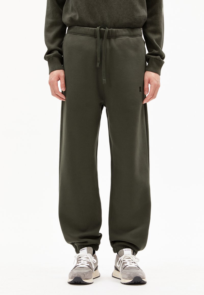 Olijfgroene joggers met een trekkoord in de taille, elastische boorden, zachte stof en subtiele logo details. Gecombineerd met grijze sneakers.