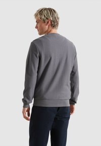 Grau strukturierter Sweatshirt mit gerippten Bündchen und Saum, ausgestattet mit einem klassischen Rundhalsausschnitt. Trägt dunkle Hosen, von hinten betrachtet.