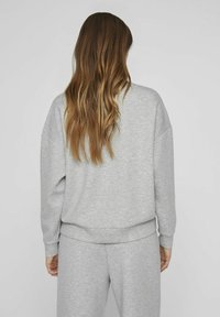 Pilkas megztinis su laisvu siluetu, ilgomis rankovėmis ir elasticinėmis rankovėmis. Minkšta medvilnės mišinio medžiaga turi paprastą, nepuošni dizainą.