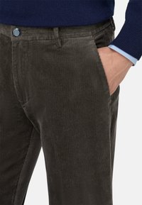 Donkergroene ribfluwelen broek met verticale ribbelstructuur, een blauwe knoopaccent op de tailleband en zijzak.