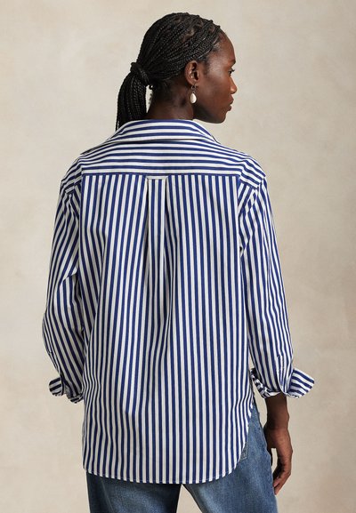 Camicia a righe in cotone blu e bianco, con piega posteriore, colletto e polsini con bottoni. Vestibilità rilassata con orlo sagomato.