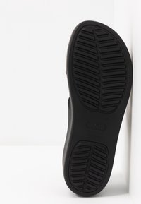 Semelle de chaussure en caoutchouc noir avec un motif de bande de roulement texturé, présentant un logo en évidence et un bord lisse et arrondi.