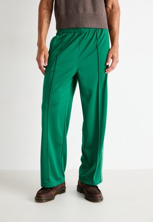 Pantalones verdes, ligeros y holgados con una cintura elástica, que cuentan con bolsillos laterales y rayas verticales en contraste a lo largo de los costados.