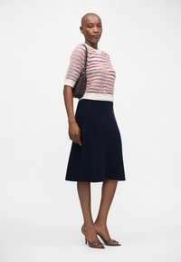 Jasnoróżowy i biały sweter w paski, granatowa spódnica o kształcie dzwonu oraz ciemne sandały na obcasie. Na ramieniu niesiona jest mała ciemna torebka.