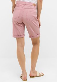 Shorts en denim rose avec ourlets retroussés, deux poches arrière et une étiquette beige sur la ceinture, offrant une texture lisse et douce.