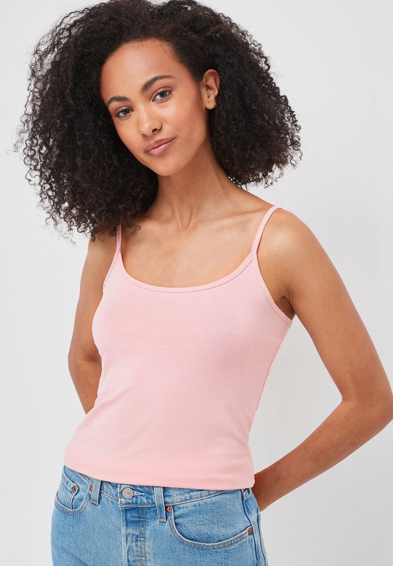 Débardeur ajusté rose clair avec des bretelles étroites, en coton doux, présentant un décolleté arrondi et une texture lisse, associé à un jean en denim bleu.