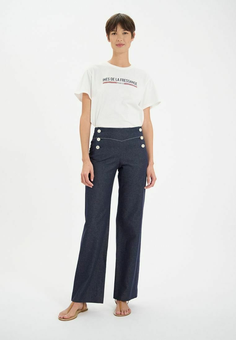 Pantalons taille haute bleu marine avec boutons à l'avant, jambes larges et texture lisse, associés à un t-shirt graphique blanc et des sandales.