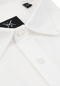 Biała bawełniana koszulka polo z klasycznym kołnierzykiem, z pojedynczym przezroczystym guzikiem przy szyi i czarną wewnętrzną metką.