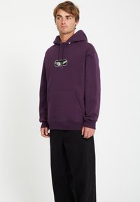 Paarse hoodie met een voorzak, trekkoorden en een grafisch logo. Gecombineerd met zwarte broeken, met een relaxte pasvorm en een zachte textuur.
