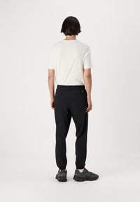 Hvid bomulds t-shirt og sorte joggers med elastisk talje og elastiske manchetter. Grå sportsko med brune accenter. Ingen synlige logoer.