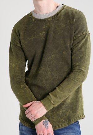 Camisa de manga larga verde oliva hecha de una tela suave con un aspecto desgastado y texturizado. Diseño de cuello redondo con ligeros detalles de desgaste.