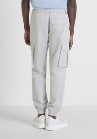 Pantalons cargo gris clair avec des poignets élastiques, plusieurs poches latérales et une coupe décontractée, fabriqués dans un tissu doux et respirant.