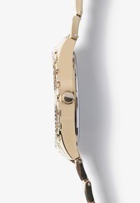 Montre-bracelet dorée avec un boîtier rond, au design minimaliste, et un bracelet en métal argenté. Elle possède une couronne texturée et une lunette lisse.