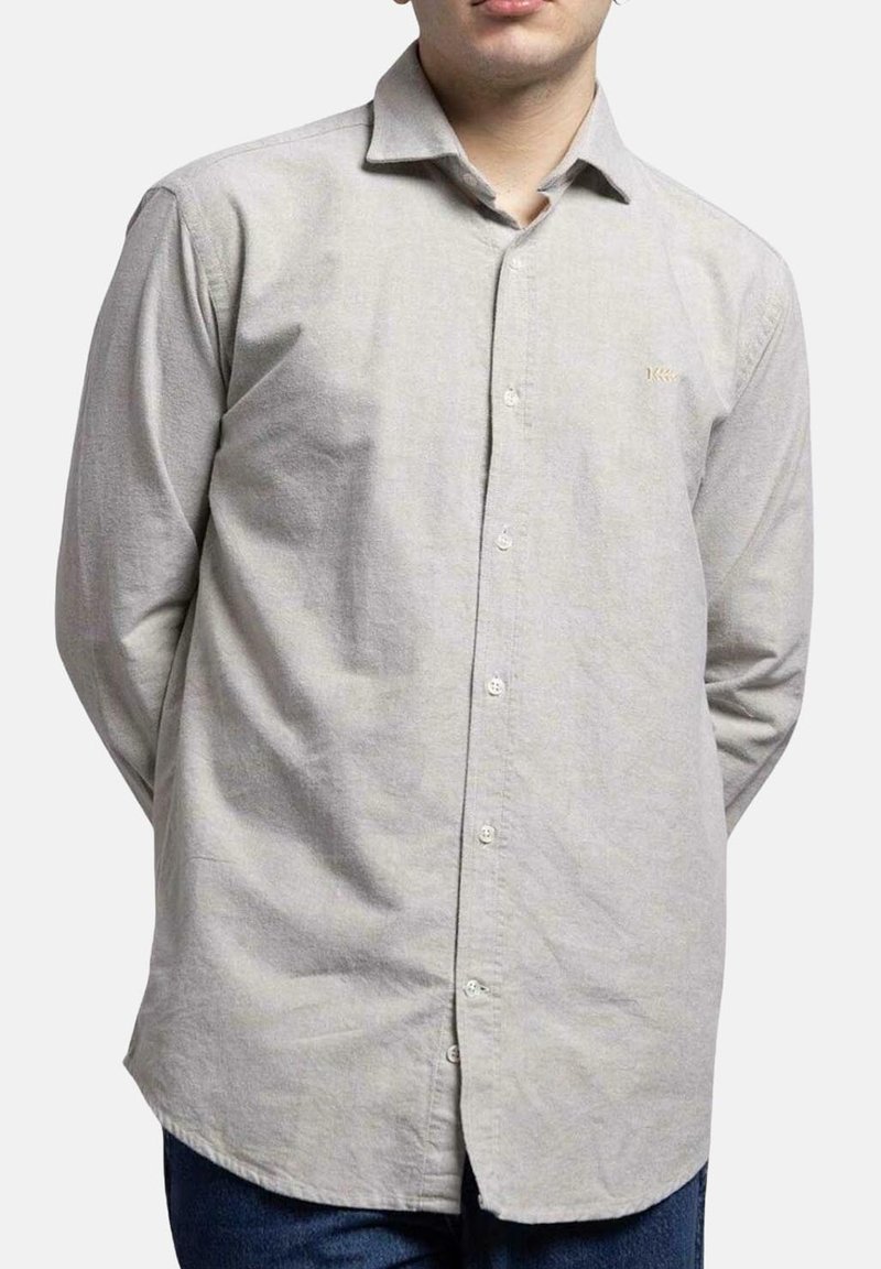 Camisa abotonada de color gris claro, hecha de una tela texturizada, que presenta un cuello, mangas largas y un dobladillo ligeramente curvado. Se observa una marca simple.