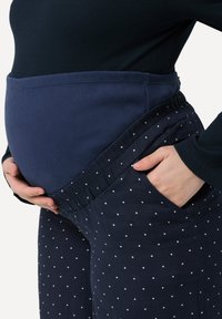 Pantaloni da maternità blu navy con pois, vita elastica e tasche laterali, abbinati a una maglia blu navy a coste che mette in evidenza il pancione.